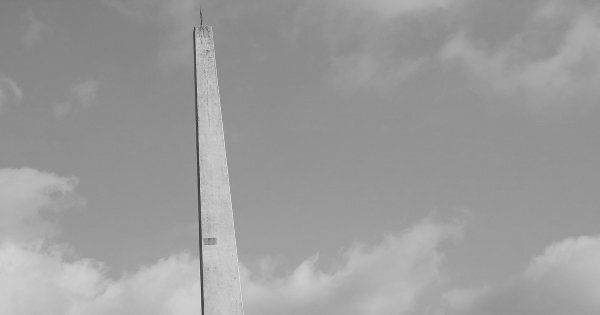 雲のある空を背景に、避雷針が取り付けられた塔が立つモノクロ写真