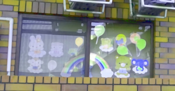 ベランダに面する窓にウサギ、サル、クマ、コアラ、風船、虹などのかわいいイラストが貼り付けられたレンガ調タイルの住宅